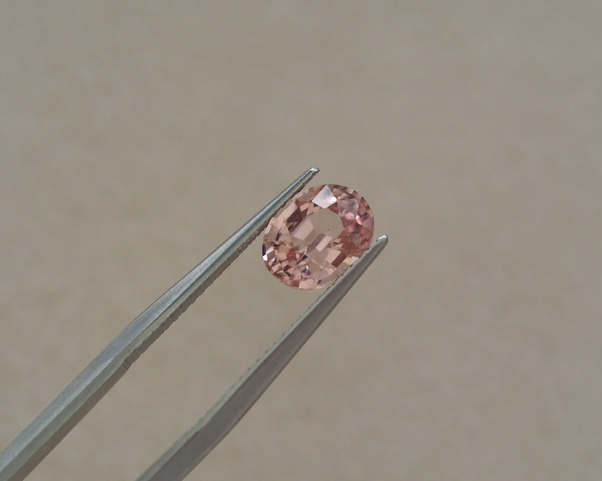 A round pink gemstone held between metal tweezers against a plain beige background.