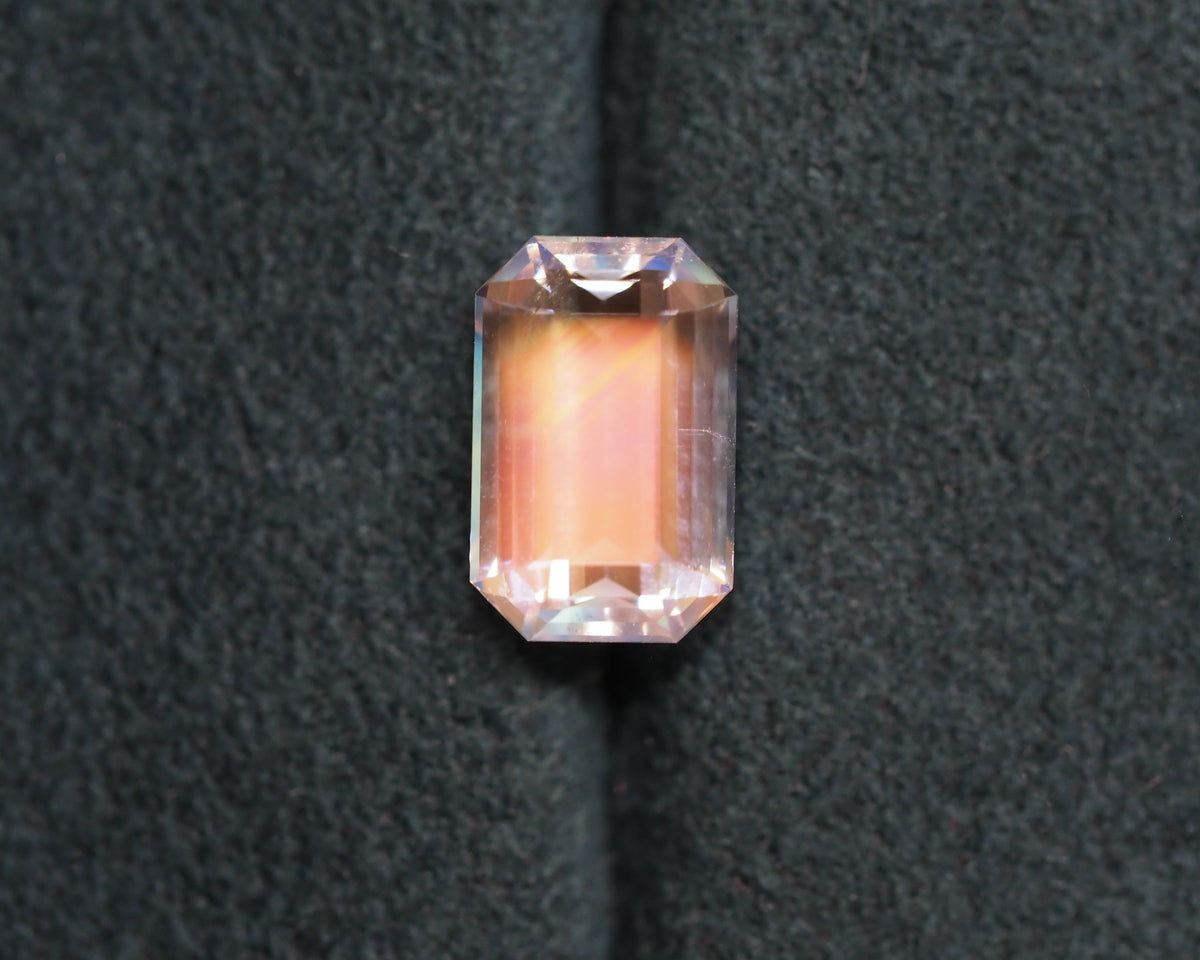 A rainbow moonstone emerald cut sits in front of a green velvet background