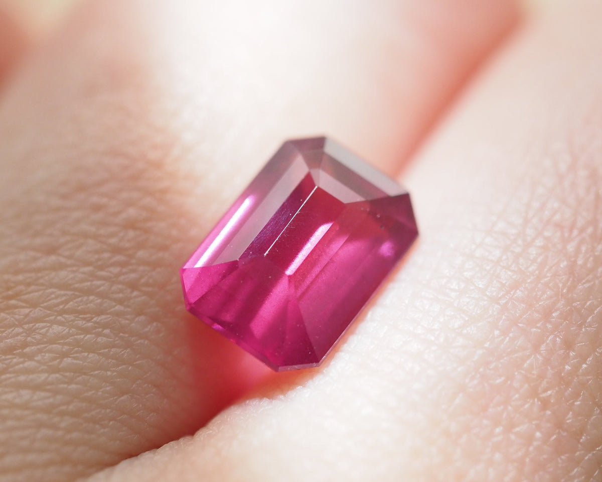 A close-up of a faceted rectangular pink Rhodolite resting between fingers.