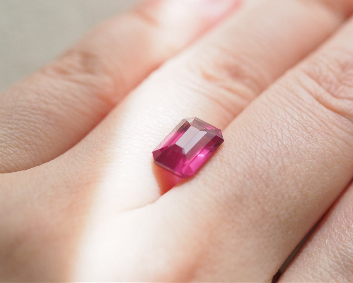 A close-up of a hand placing a rectangular pink rhodolite between fingers.