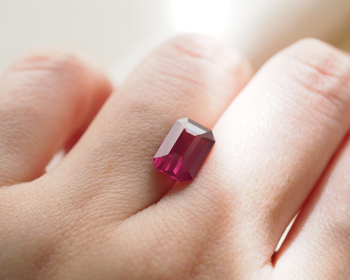 A close-up of a hand placing a faceted rectangular pink rhodolite.