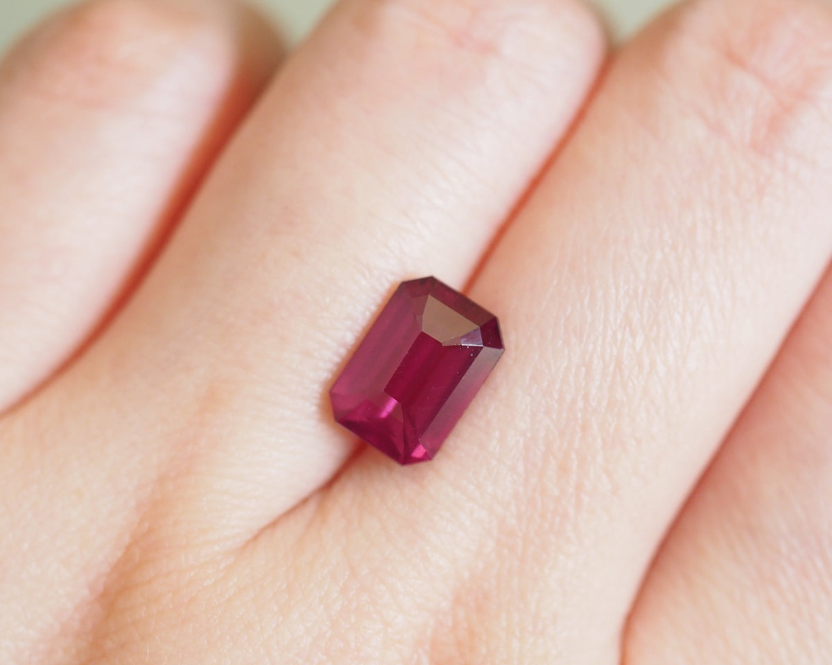 A rectangular emerald-cut deep pinkish-red rhodolite worn on a finger.