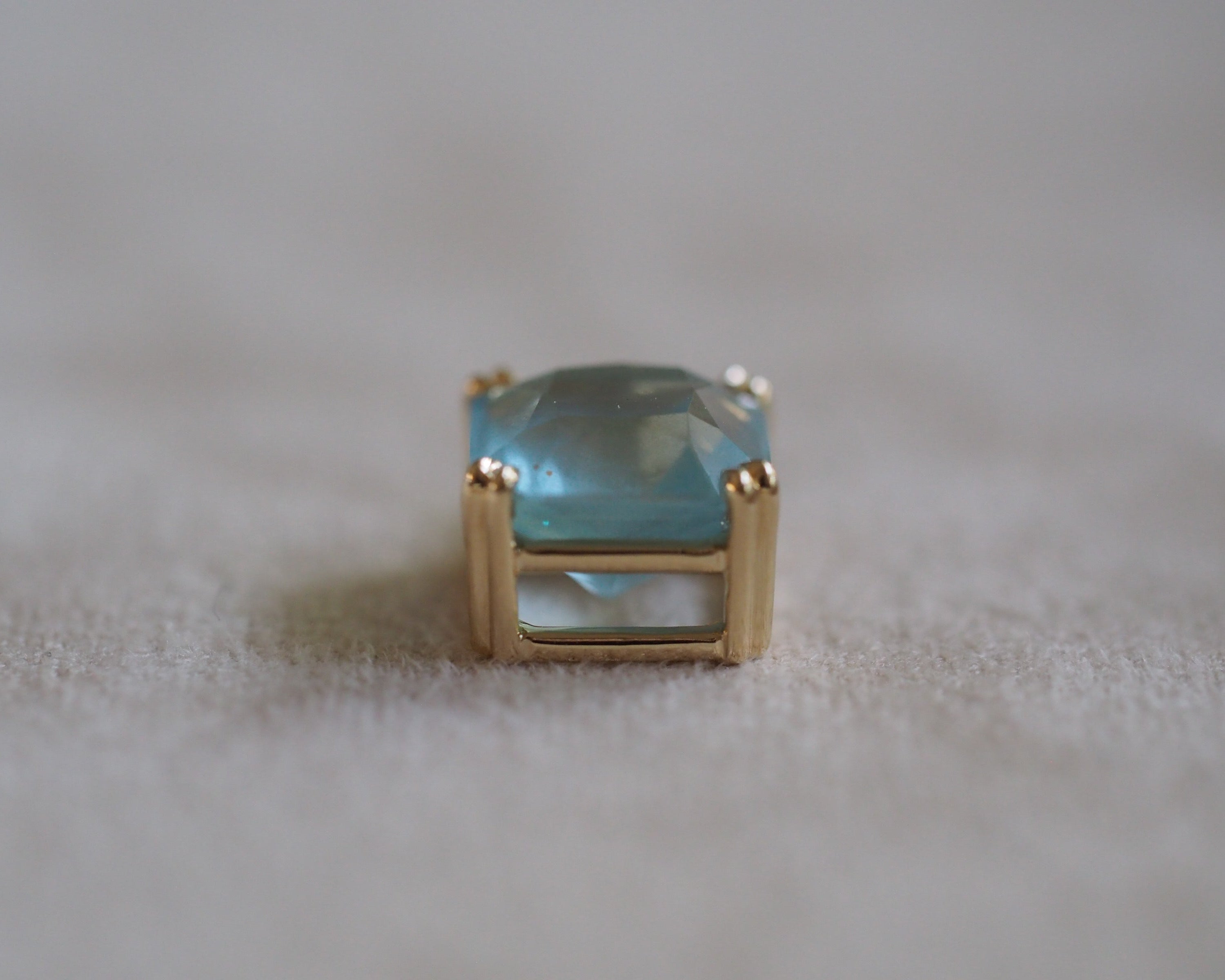 Bottom of Carolyn Asscher Aquamarine pendant in front of a beige background