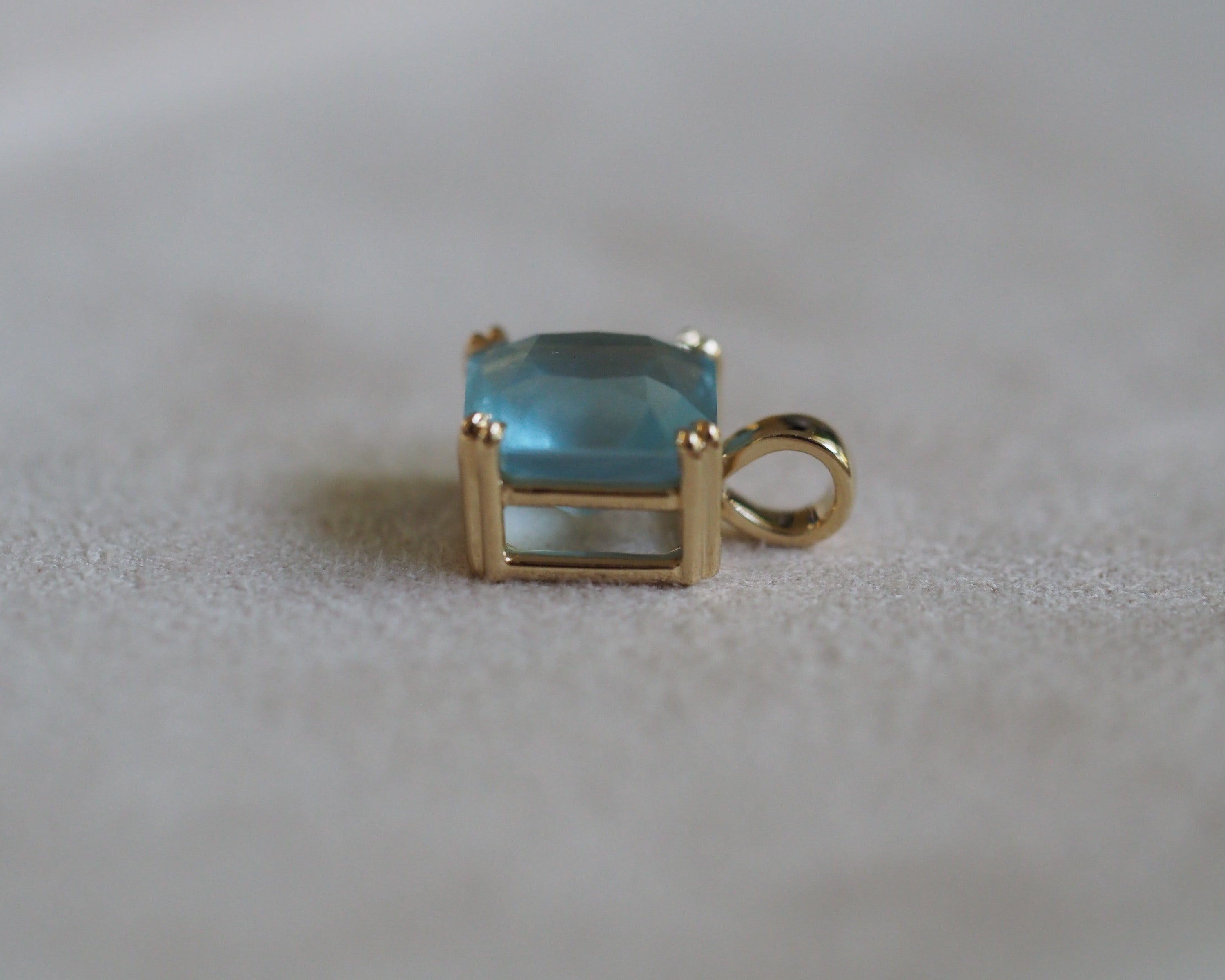 Side of Carolyn Asscher Aquamarine pendant in front of a beige background