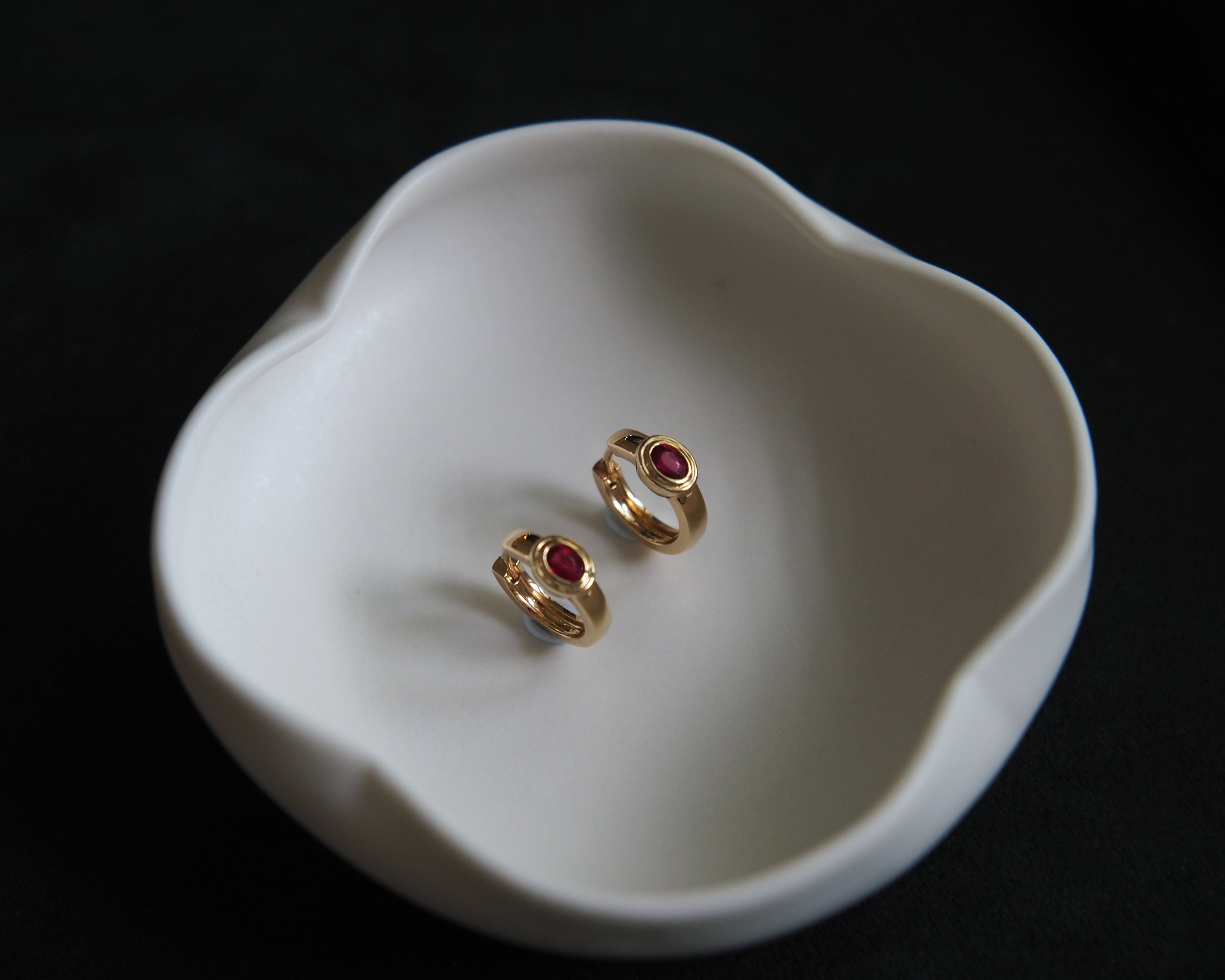 Two gold rings with red gemstones on a white dish against a black background