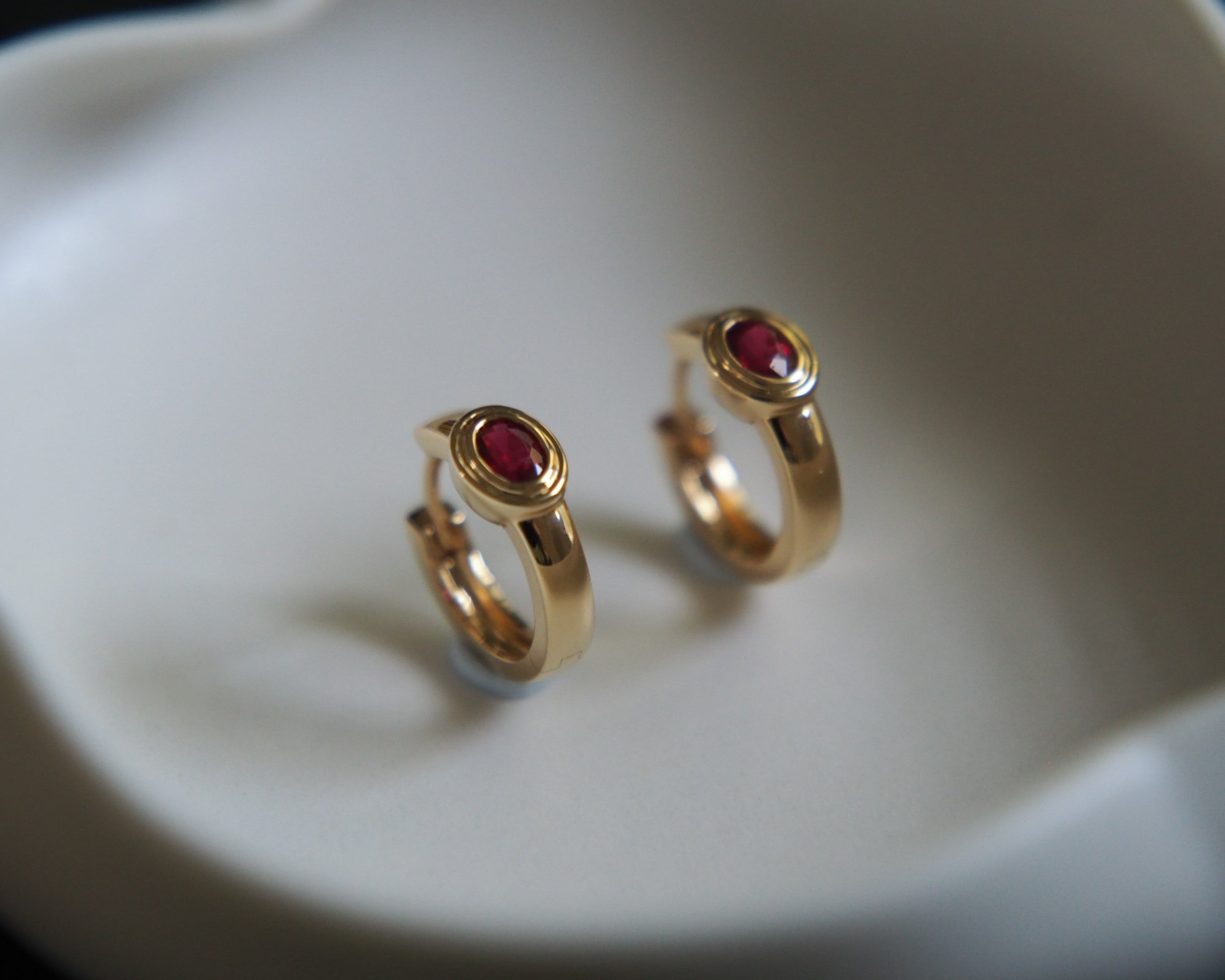 Gold hoop earrings with red gemstones on a white dish