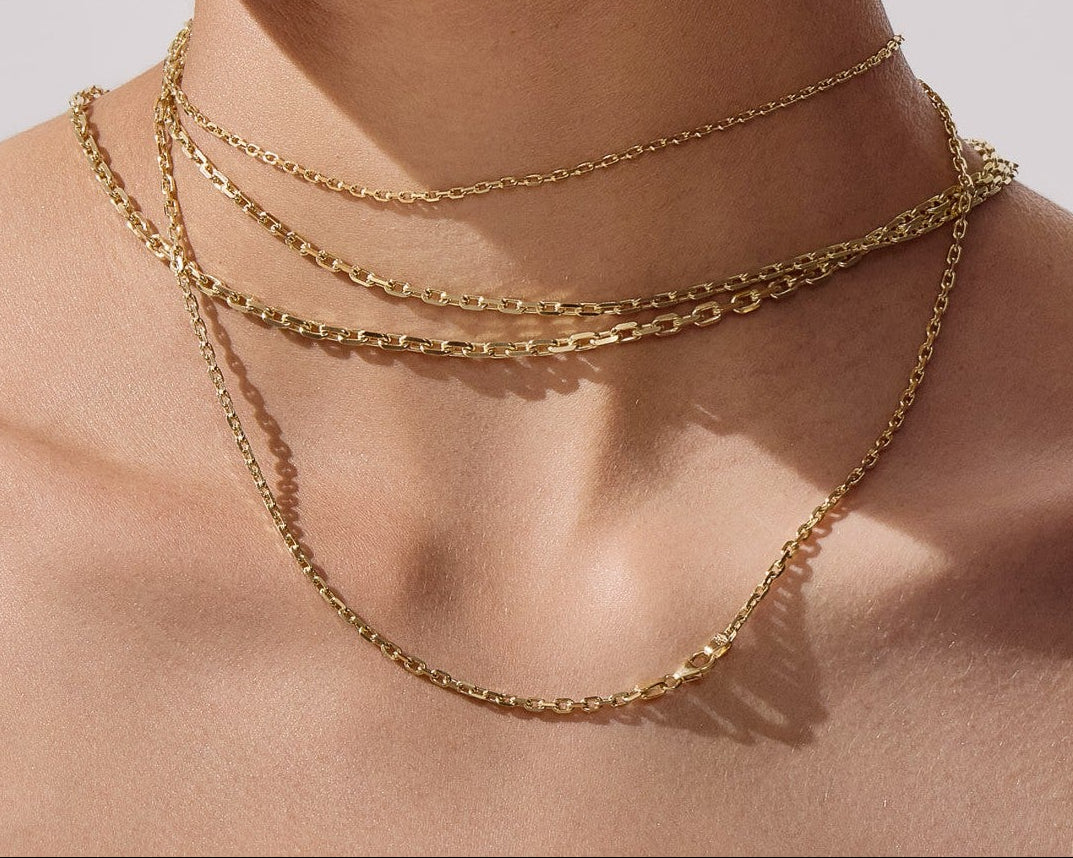 Close-up of a woman wearing gold necklaces and earrings against a neutral background