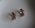 Gold hoop earrings with heart-shaped purple gemstones on a gray background