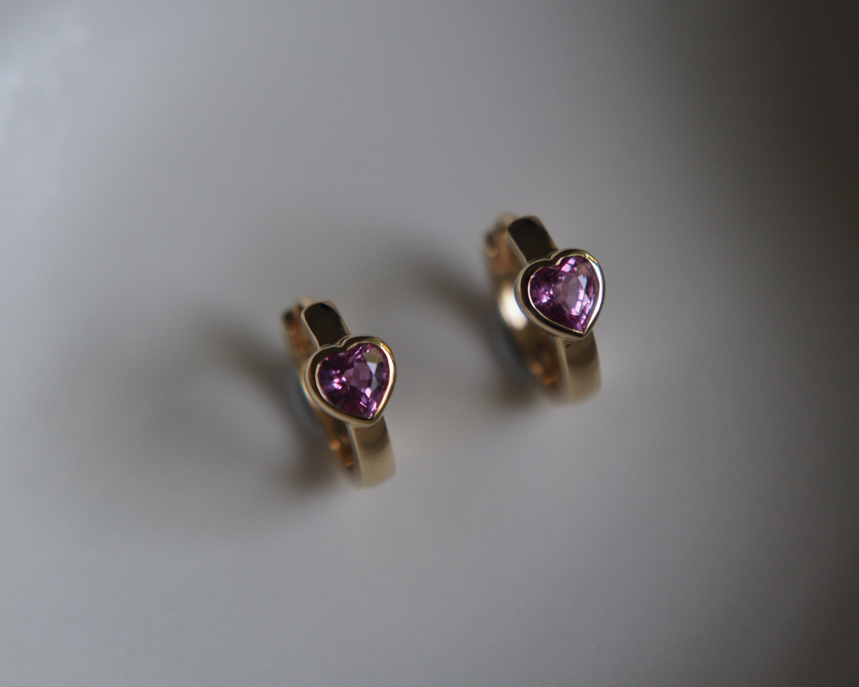 Gold hoop earrings with heart-shaped purple gemstones on a gray background