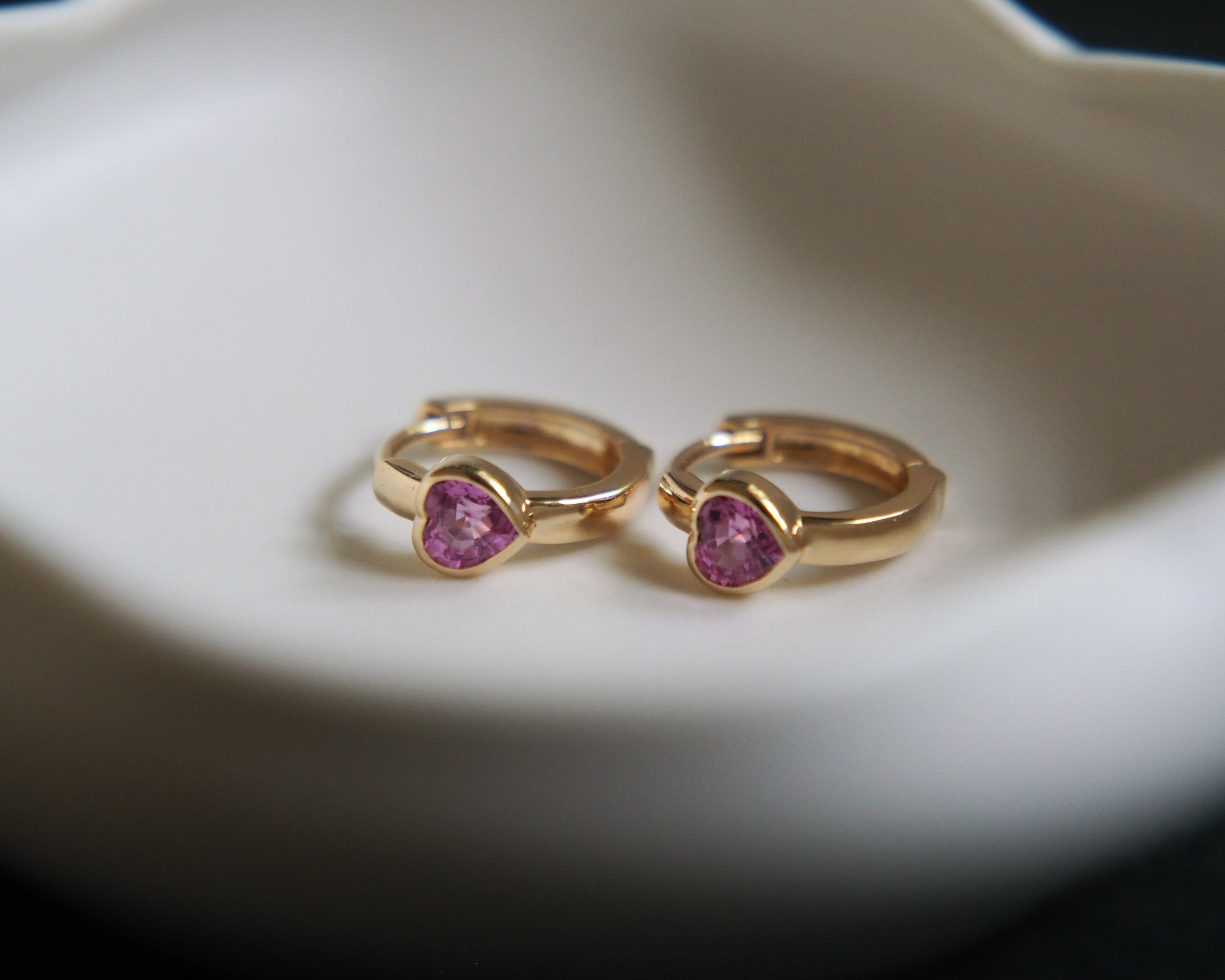 Gold hoop earrings with pink gemstones on a white dish