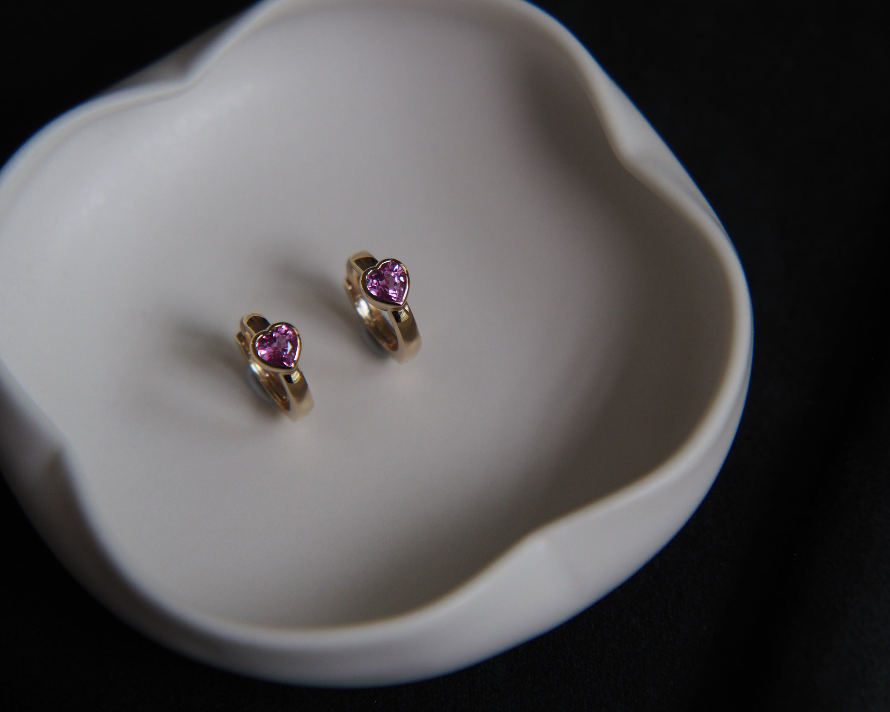 Gold heart-shaped earrings with pink gemstones on a white dish.