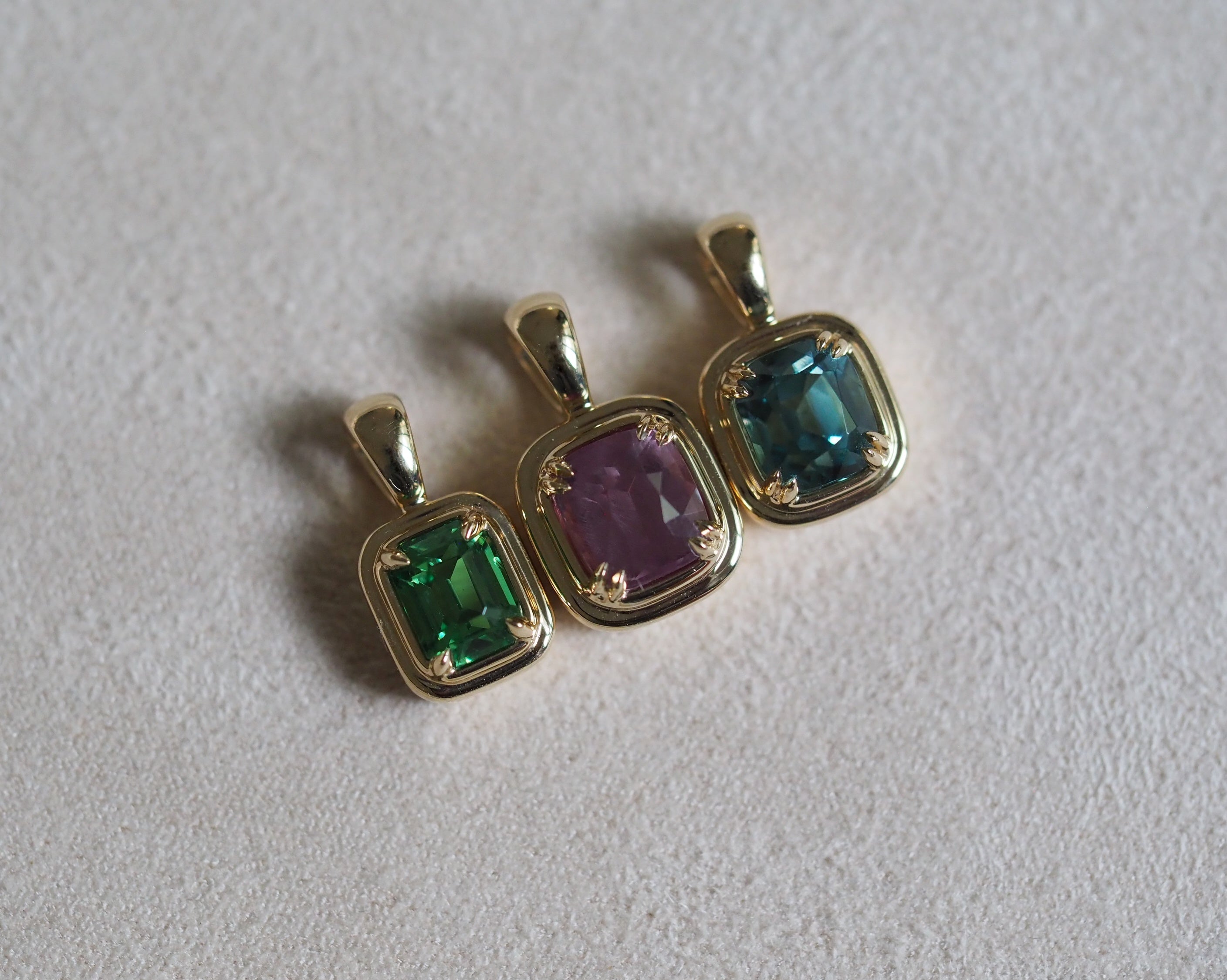 Two Juno tourmaline and garnet pendant with Robyn tsavorite pendant, arranged on a textured light gray surface.
