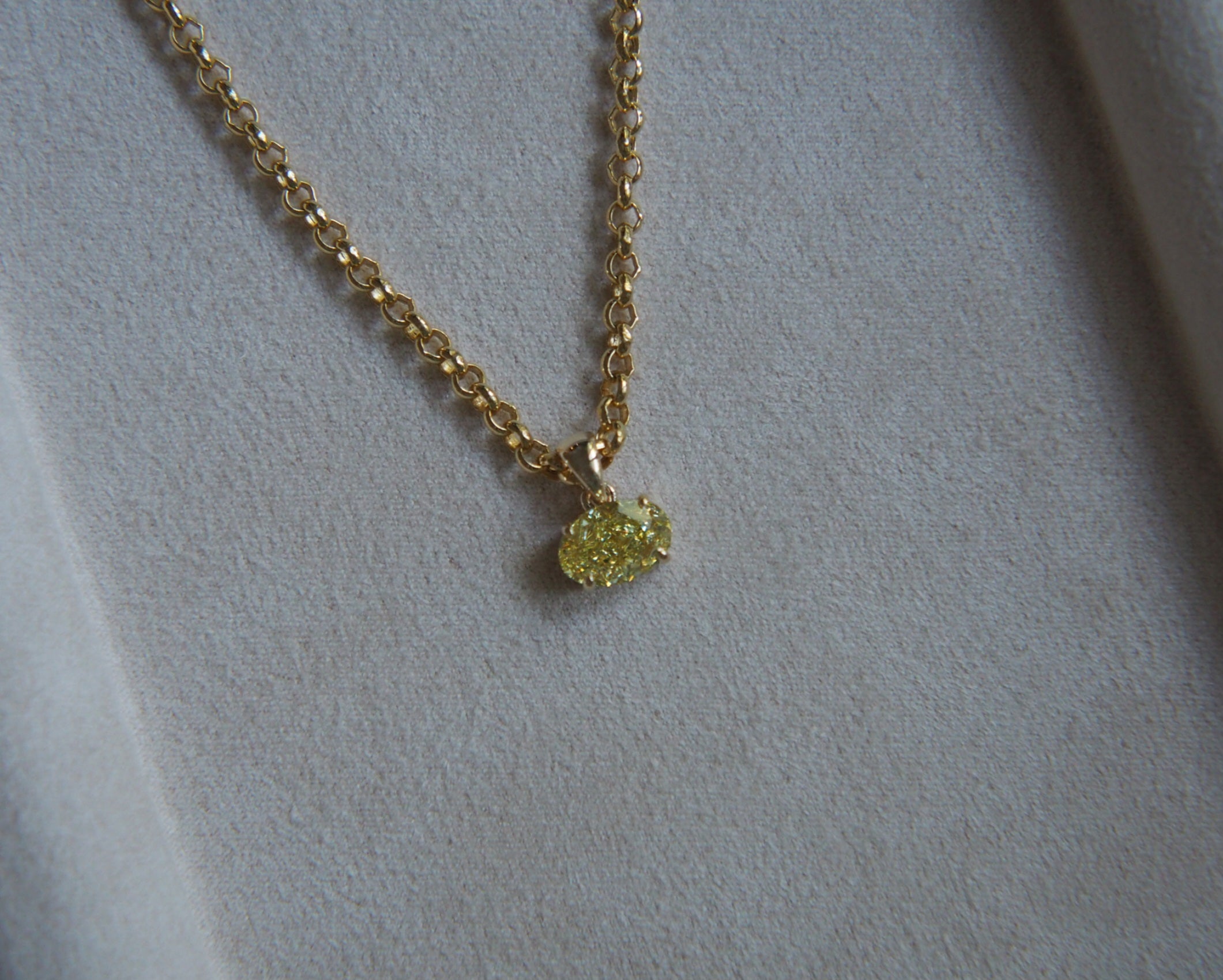 Oval yellow diamond on a gold chain in front of a beige background