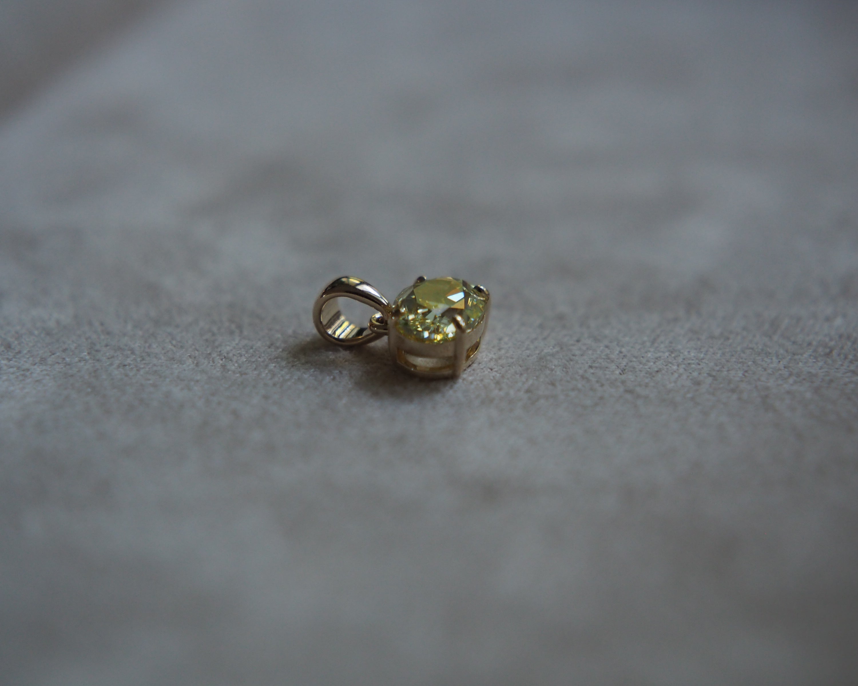 Side of a yellow oval diamond pendant on a beige background