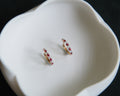 Pair of gold earrings with red gemstones on a white dish.
