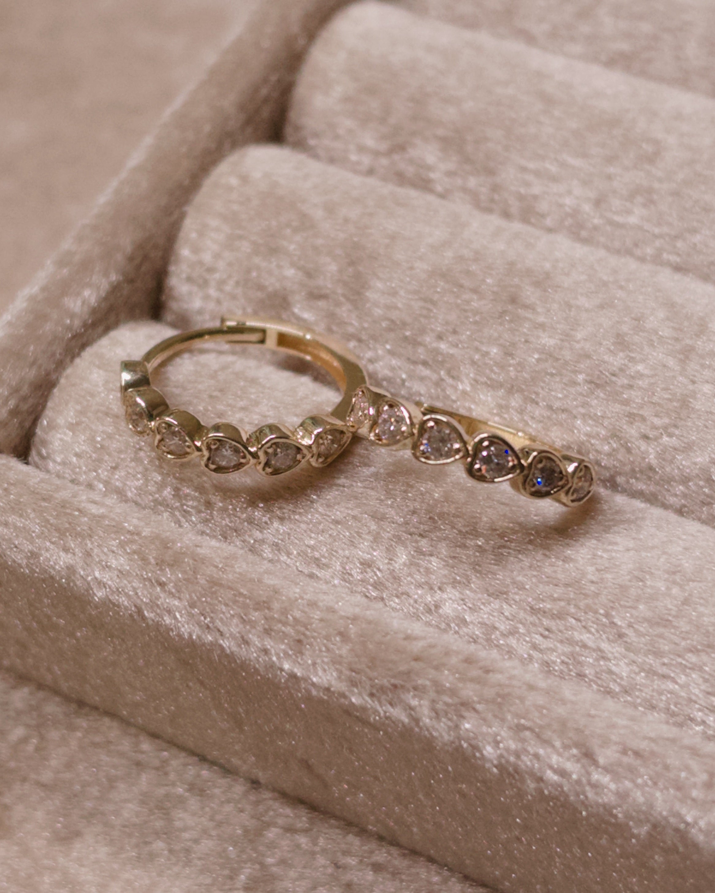 Gold heart hoops with small diamonds on a beige velvet surface