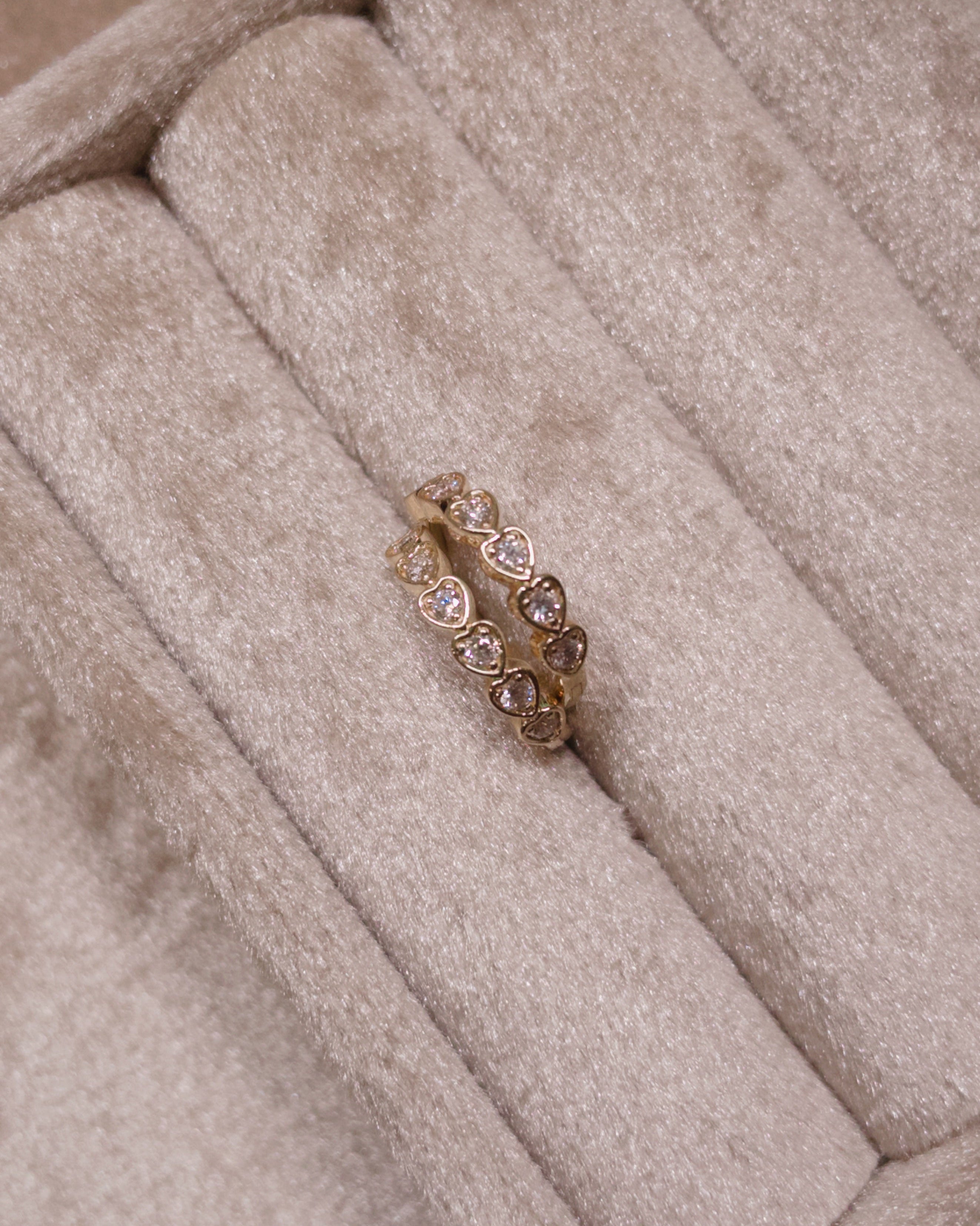 Gold heart hoops with embedded stones on a beige cushioned surface
